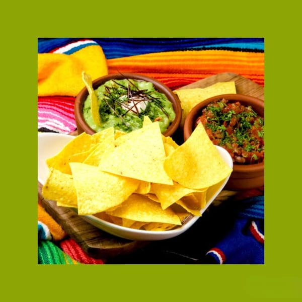 Crispy tortilla chips with bowls of fresh guacamole and salsa on a colorful Mexican blanket.