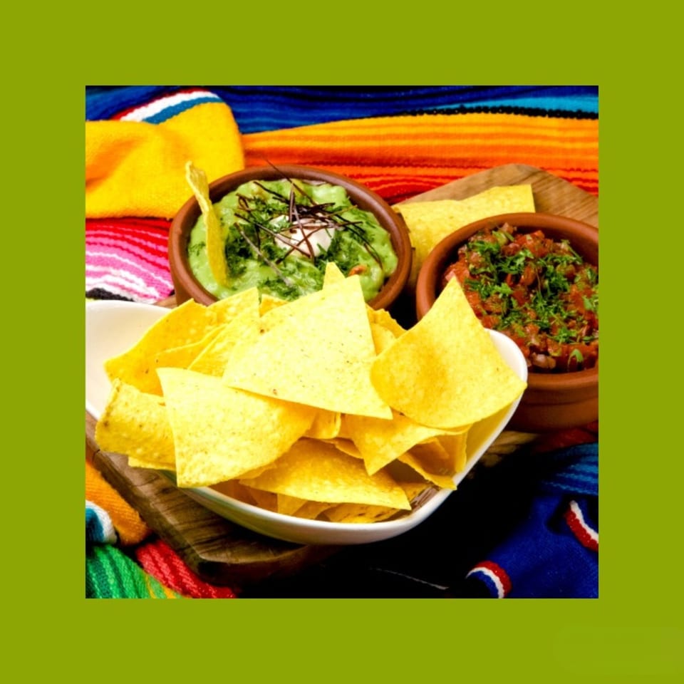 Crispy tortilla chips with bowls of fresh guacamole and salsa on a colorful Mexican blanket.