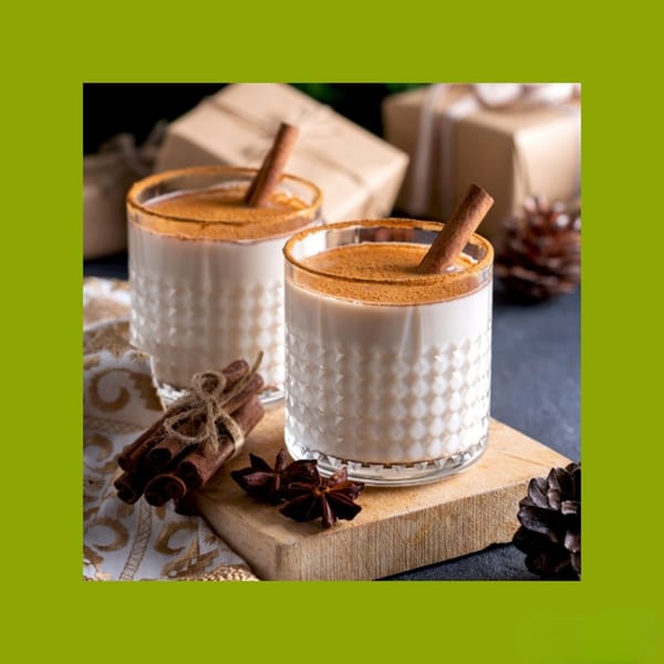 Two glasses of horchata, garnished with cinnamon sticks and powder, on a wooden board with spices.