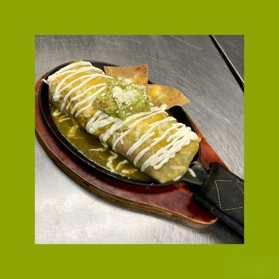 A sizzling La Familia Callejas Mexican Food burrito covered in cheese, sour cream, and guacamole.