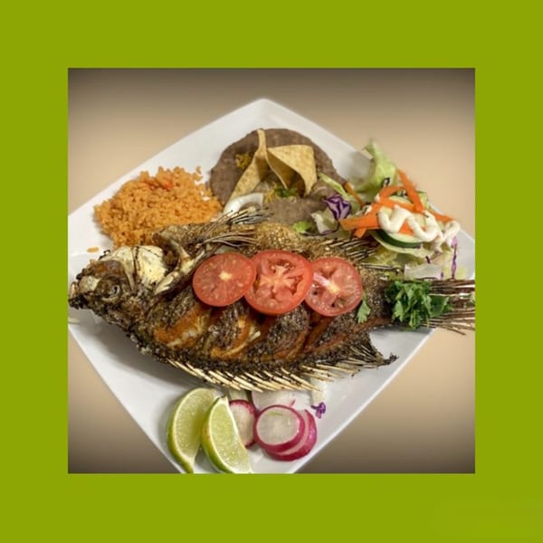 Fried whole fish with tomato slices, rice, beans, salad, lime, and radish on a white plate.