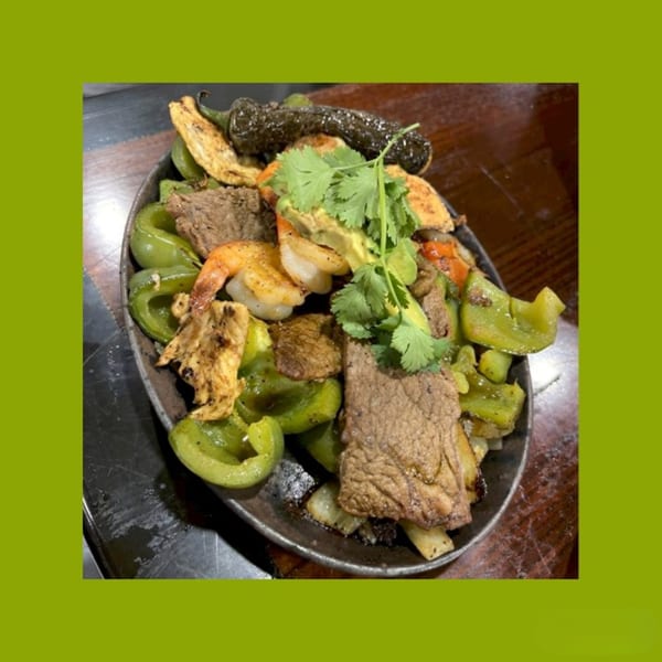 Sizzling fajitas with steak, shrimp, chicken, green peppers, onions, and cilantro in a hot skillet.